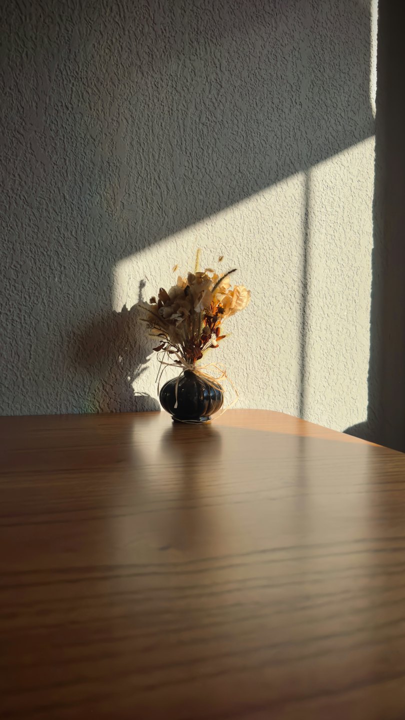 Flores secas en un jarrón de cerámica negra sobre una mesa.
