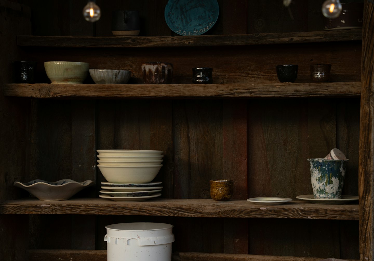 Cuencos, platos y tazas de cerámica hechos a mano en estantes rústicos de madera.