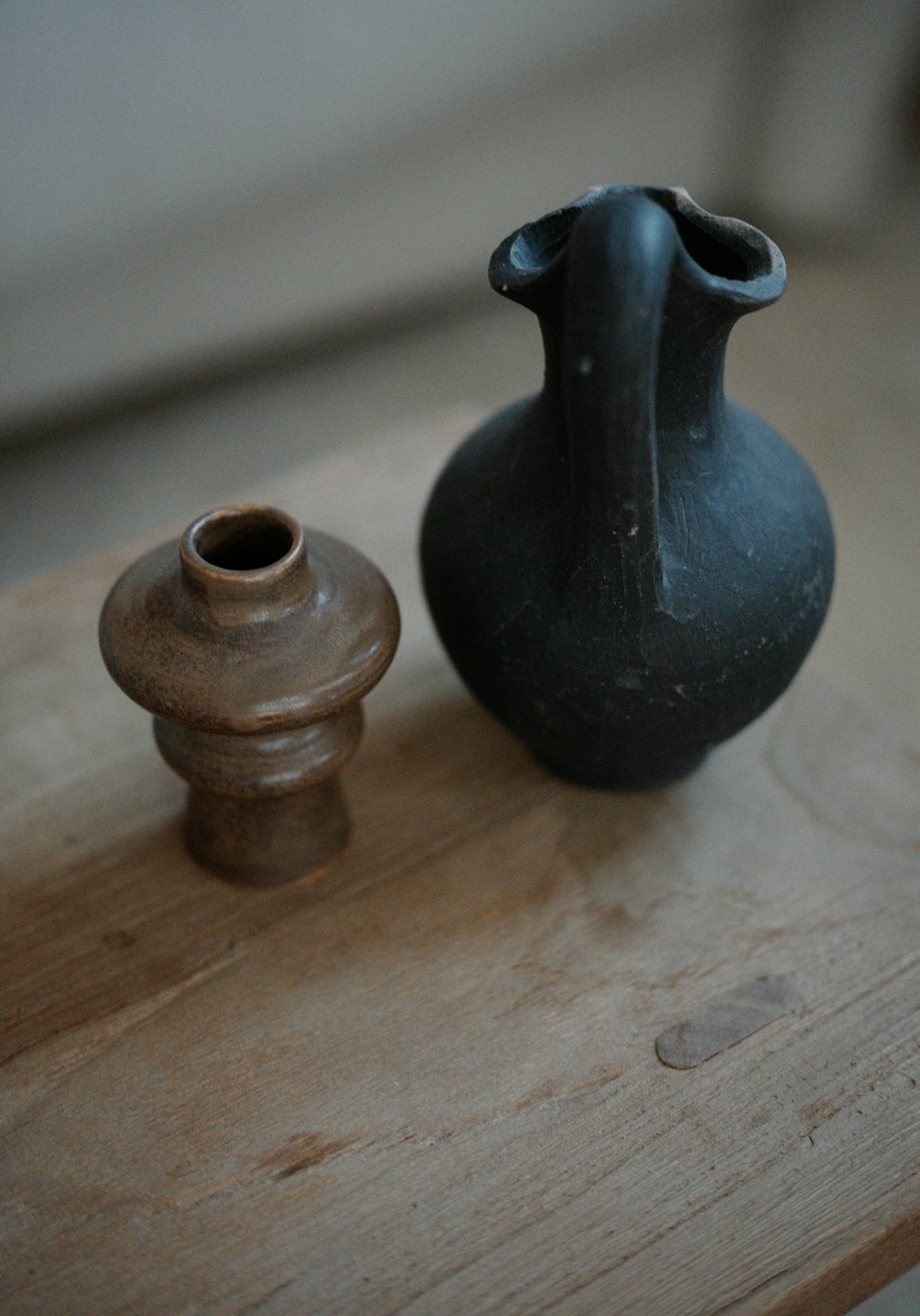 Jarra de cerámica gris oscuro y tarro apilado marrón sobre mesa de madera.