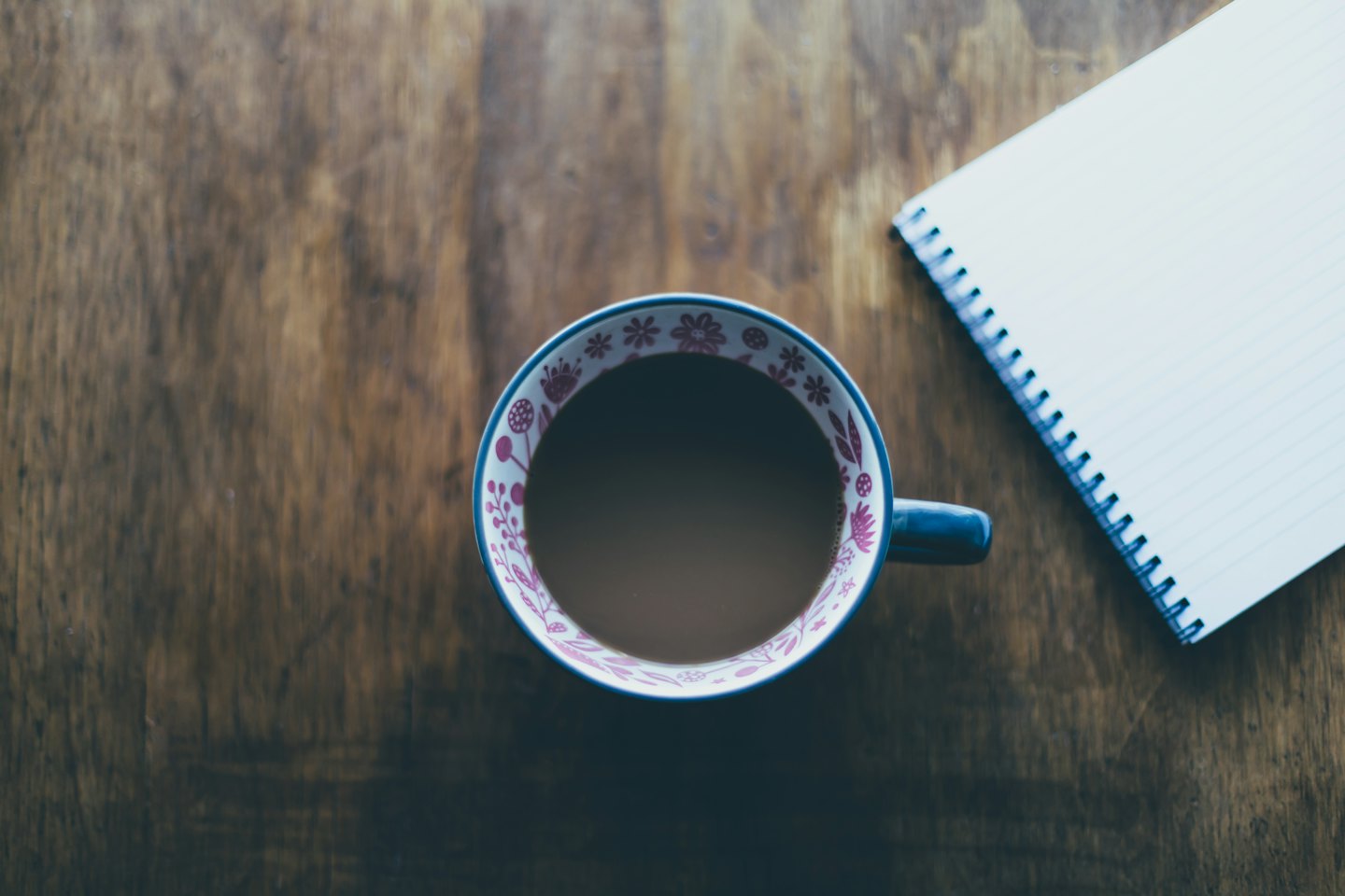 Taza de café estampada junto a un cuaderno sobre un escritorio de madera.